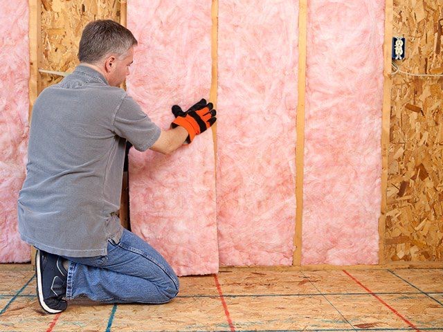 Installer fitting fiberglass batt insulation into a stud wall