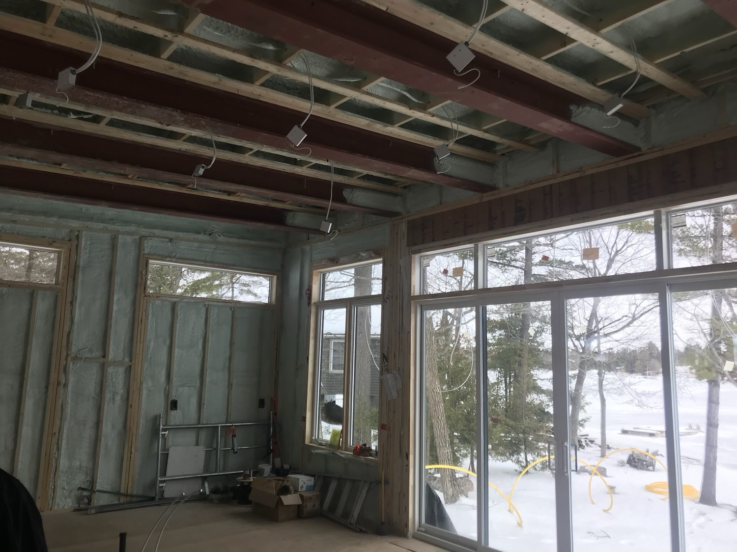 Great room under construction, insulated, with large windows looking out onto snow
