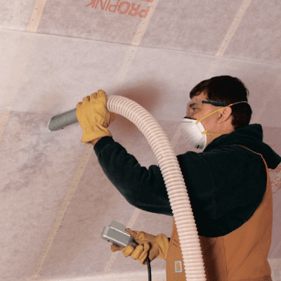 Installer injecting blown fiberglass insulation into a wall cavity through a hose