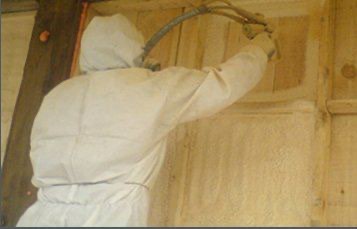 Applicator in a protective suit spraying polyurethane foam onto a wall
